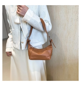 Brown leather hobo bag styled on a white jacket with focus on the metal buckles