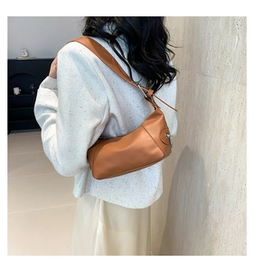 Brown leather baguette shoulder bag shown on shoulder of model in tweed blazer