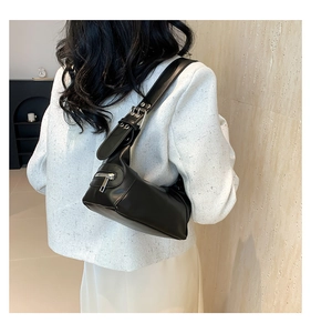 Side view of black leather underarm bag with silver zipper on white tweed jacket