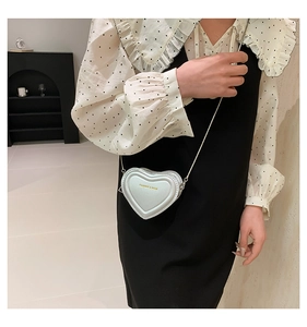 Close-up of white heart-shaped crossbody bag with silver chain and fashion lettering