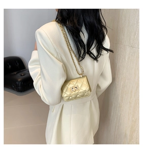 Detailaufnahme einer mini goldfarbenen Stepptasche mit Kette über einem weißen Anzug