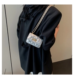 Detail der silbernen Stepptasche mit goldener Kette am Model in schwarzem Anzug