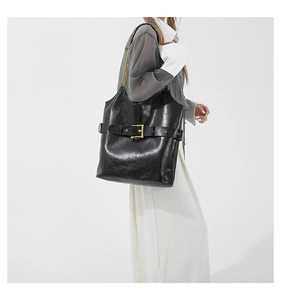 Detalle de bolso tote de cuero negro brillante con hebilla dorada y correa de cadena