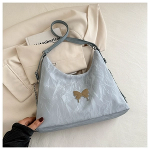 Dettaglio della borsa hobo azzurra con trama a pieghe ed emblema a farfalla