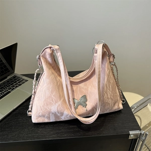 Borsa a spalla plissettata rosa con farfalla argentata e tracolla a catena su tavolo