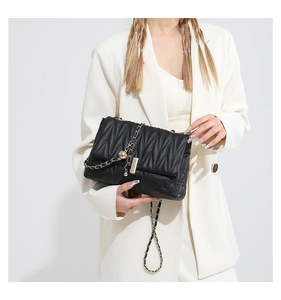 Detailed view of black pleated shoulder bag with gold chain strap on white blazer