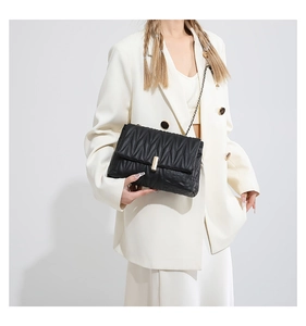 Detail of black pleated chain bag with gold buckle on white oversized blazer model