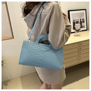 Modella che indossa una borsa azzurra con motivo a coccodrillo e manico rotondo