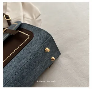 Macro shot of bag bottom with denim texture, brown leather edges and gold protective studs