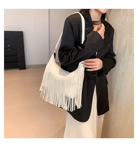 Détail d'un sac hobo blanc à longues franges porté à l'épaule sur une veste de blazer