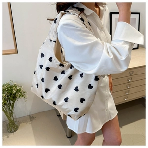 Detail of beige canvas hobo bag with black heart prints on a model in a minimal setting
