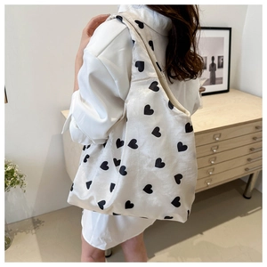 Close-up of beige canvas tote bag featuring black heart prints and wide shoulder strap