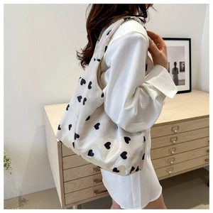 Detail of cream canvas tote bag with black heart patterns worn on shoulder for commuting