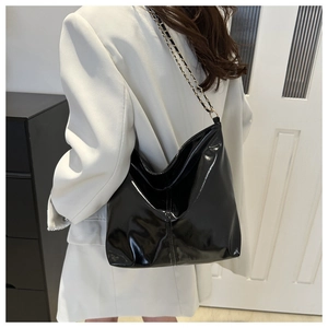Detail of glossy black patent leather tote with metal woven chain strap for women