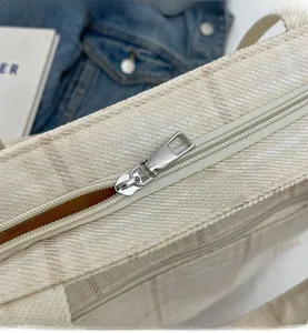 Detail of the smooth silver zipper closure on a cream checkered woven tote bag