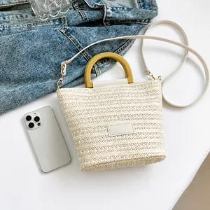 Detalle del bolso tipo tote de paja tejida con asa redonda de madera y correa de hombro