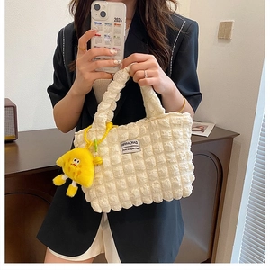 Detalle del bolso tote crema con textura de palomitas, etiqueta y colgante amarillo