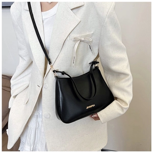 Dettaglio di una borsa a tracolla in ecopelle nera con logo dorato su un blazer bianco
