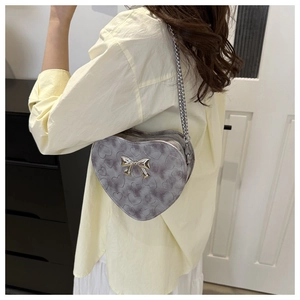 Détail du sac bandoulière argenté en forme de cœur avec gaufrage et nœud métallique