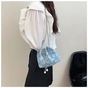 Detail of light blue bucket bag with 3D floral texture and elegant pearl tassels