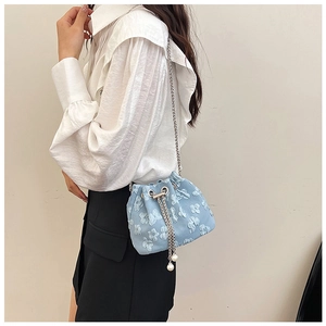 Detail of light blue bucket bag featuring 3D floral texture and pearl drawstring accents