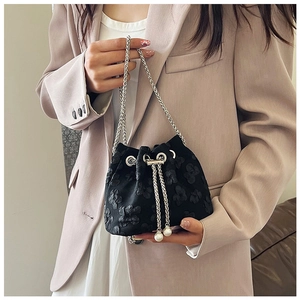 Detail of black drawstring bucket bag with floral texture, silver chain, and pearl accents