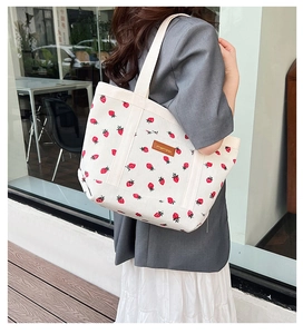 Detail of white corduroy tote bag with red strawberry pattern and brown leather logo tag