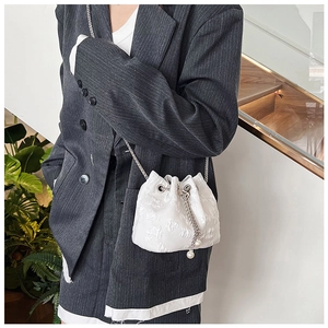Detailed view of white embossed bucket bag featuring silver chain and pearl drawstrings