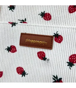 Close-up of white corduroy fabric with strawberry print and a brown leather logo patch
