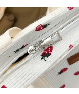 Close-up of smooth metal zipper and sweet strawberry print on white corduroy bag