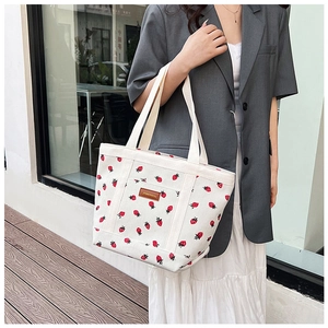Detailed view of strawberry print on corduroy tote bag with leather logo patch