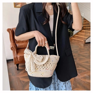 Détail du sac cabas en paille crème avec broderie colorée et accent de nœud en dentelle