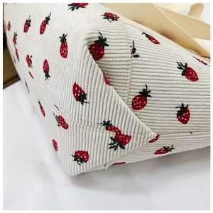 Detail of strawberry print on beige corduroy tote bag showing fabric texture and base