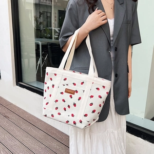 Minimalist white canvas tote bag with red strawberry print and wide handles in outdoor setting