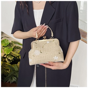 Dettaglio della borsa intrecciata con ricami floreali bianchi e manico di perle