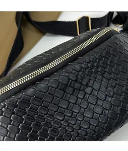 Dettaglio della cerniera dorata e trama intrecciata su borsa da petto nera da donna