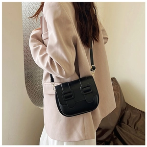 Détail d'un sac bandoulière noir minimaliste avec boucles dorées sur un blazer beige