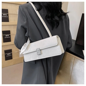 Vue détaillée du sac baguette blanc avec boucle en strass porté sur un blazer gris
