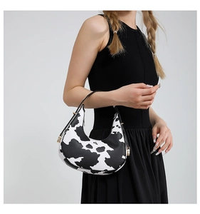 Detail of a chic half-moon handbag with black and white cow print and gold hardware buckle