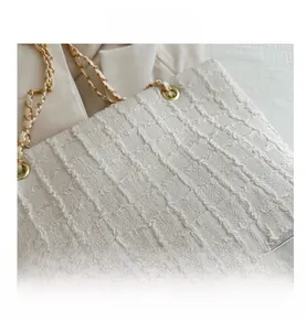 Close-up of white quilted tote bag featuring gold chain strap and textured finish