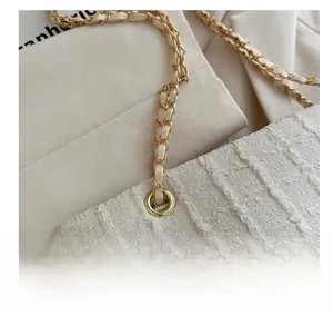 Detail of cream shoulder bag with gathered texture and woven gold chain strap