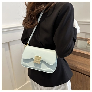 Détail du sac en cuir bleu clair avec fermoir ours doré et bord ondulé sur l'épaule