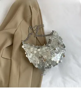 Close-up of silver sequin crescent bag with metallic chain strap on khaki fabric