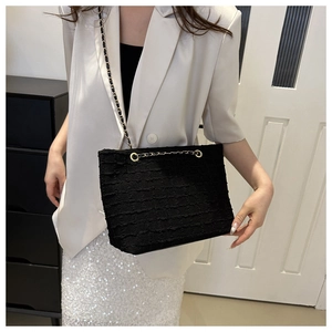 Detail of black textured tweed shoulder bag with gold chain strap on beige blazer