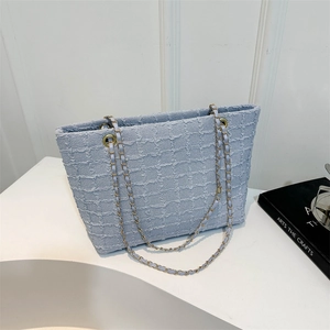 Light blue tweed tote bag with gold chain strap on minimalist white display stand