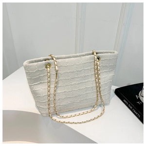Detailed macro view of cream tweed texture and gold chain strap on chic tote bag