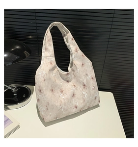 Détail du sac cabas en toile beige avec motif floral blanc posé sur une table blanche