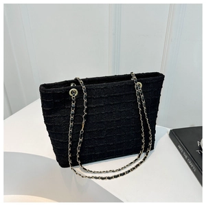 Close-up of black woven tweed tote bag with gold chain straps on minimalist background
