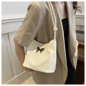Detalle del bolso de hombro crema con adorno de mariposa plateada y correa de cuerda anudada