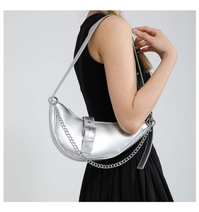 Primer plano del bolso media luna plateado con cadena decorativa sobre vestido negro